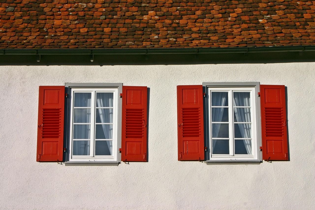 Façade claire avec fenêtres et volets rouges sous un toit en tuiles